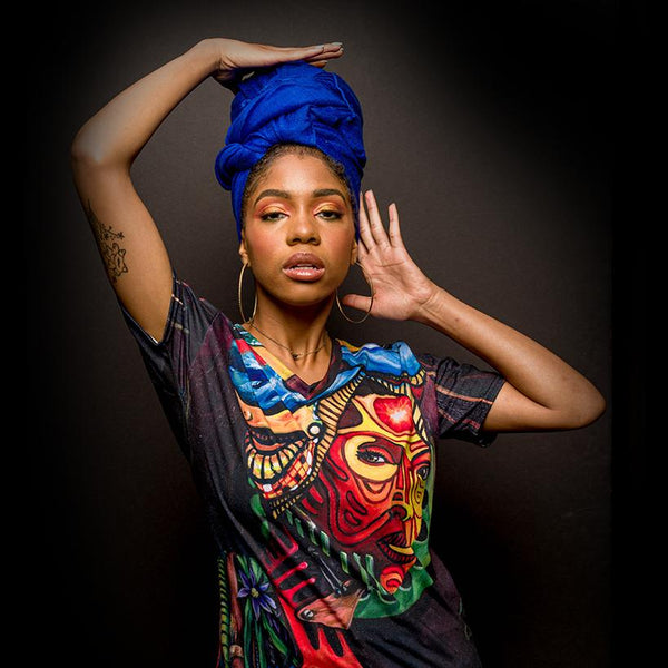 African-American woman wearing a vibrant blue headwrap and a vibrant colorful painting tshirt.